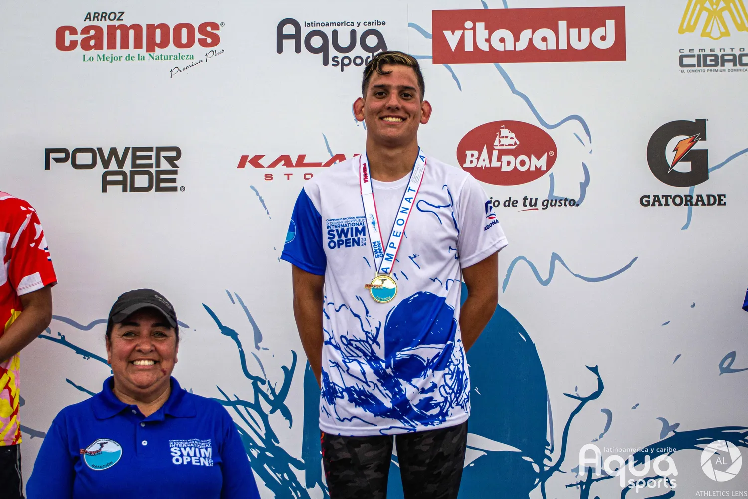 Podio de competencia: atleta con medalla de oro junto a una integrante del equipo técnico.